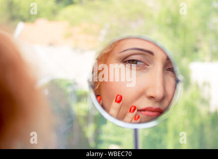 Donna che guarda, esaminando la sua nasolabial fold, i suoi primi segni di invecchiamento. La bellezza e il concetto di cura del viso di una donna matura. Foto Stock