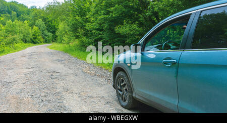 Suv sulla vecchia strada forestale. blu ciano veicolo parcheggiato su asfalto screpolato strada in salita tra alberi. Vista da Driver e porta lo specchietto laterale. perso d Foto Stock