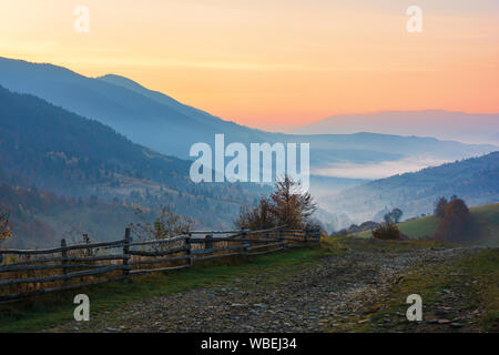 Incredibile splendida zona rurale all'alba. mattina nei Carpazi. la nebbia in valle lontano. staccionata lungo la strada di ghiaia Foto Stock