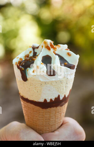Gelato alla vaniglia con cioccolato e pezzi e nocciola nelle mani di una donna Foto Stock