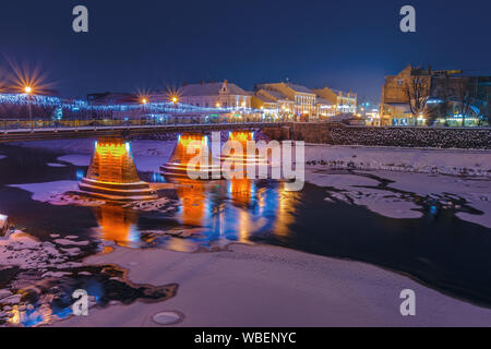 Uzhgorod, Ucraina - 06 gen, 2019: Alba d'inverno in città. meraviglioso paesaggio urbano con la luce della città sul ponte. lanterna sul terrapieno. riflessione su Foto Stock