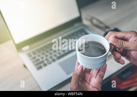 Imprenditori che stanno sorseggiando un caffè la mattina, concentrandosi sulle tazze da caffè vi è un computer notebook sfondo vista superiore. Foto Stock