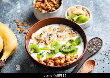 Muesli frutta yogurt ciotola con semi di chia per una sana colazione o uno spuntino. Kiwi, banana, oat granola e lo yogurt greco miscelati in un recipiente. Cibo sano Foto Stock