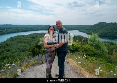 Amare giovane di 30-40 anni all'aperto avvolgente e in piedi alta su una collina con un fiume che scorre attraverso i boschi sullo sfondo Foto Stock