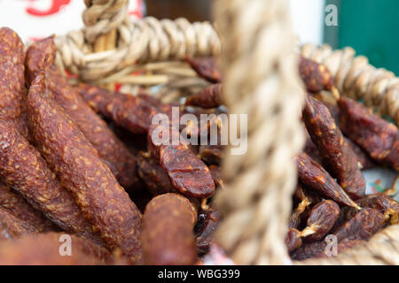 Tipiche austriache , italiano e tedesco aria salsiccia secca, cosiddetto Kaminwurzen, in un cesto in un mercato in stallo Foto Stock