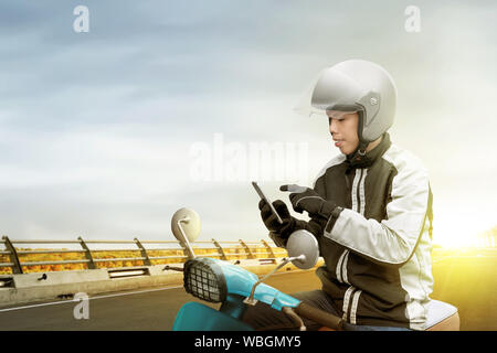 Asian motociclo taxi uomo controllo dell'ordine sul suo telefono cellulare sulla strada di città Foto Stock