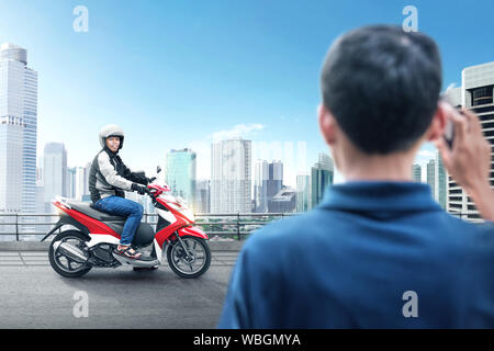 Asian motociclo taxi uomo pick up i suoi passeggeri su midtown Foto Stock