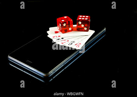 Mobile phone su sfondo nero con diverse carte da gioco e dadi rossi sul display, immagine concettuale su mobile industria del gioco Foto Stock