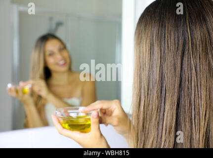 Giovane donna di applicare olio d'oliva maschera per capelli davanti ad uno specchio. Cura dei capelli concetto. Focus sui capelli. Foto Stock