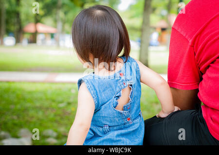 Torna padre e figlia piccola godono di vista sul parco in un parco tropicale, seduta su una panchina. I bambini e i papà insieme all'aperto. Foto Stock