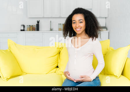 Africana incinta donna americana seduto sul divano di casa Foto Stock