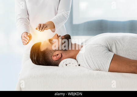 Vista ritagliata di guaritore mettendo le mani sopra la testa del giovane con gli occhi chiusi Foto Stock