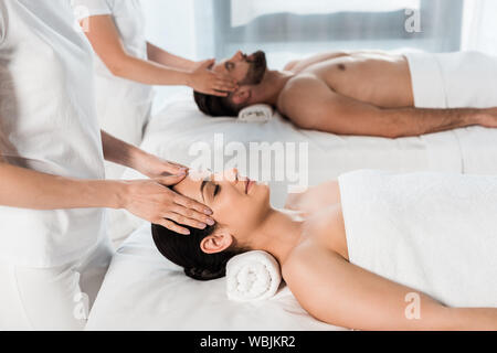 Vista ritagliata di massaggiatori facendo massaggi per donna attraente e uomo bello nel centro spa Foto Stock