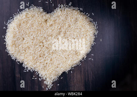 Vista dall'alto il simbolo del cuore di riso parboiled nero su uno sfondo di legno Foto Stock