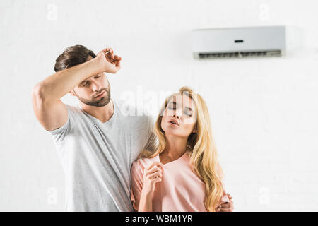 Giovane tergi fronte e che soffrono di calore sotto il condizionatore d'aria di casa Foto Stock