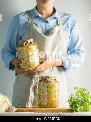 Conservazione di fermentazione crauti in vasetti di vetro nelle mani di una donna sfondo naturale. Elaborazione del raccolto autunnale. Conserve vegetariane hea Foto Stock