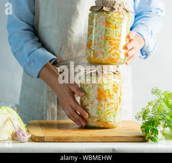 Conservazione di fermentazione crauti in vasetti di vetro nelle mani di una donna sfondo naturale. Elaborazione del raccolto autunnale. Conserve vegetariane hea Foto Stock