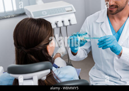 Vista ritagliata di dentista di guanti in lattice tenendo lo spazzolino denti vicino a modello e ragazza Foto Stock