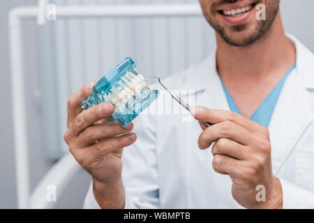 Vista ritagliata della allegro dentista holding strumento dentale e modello di denti in mani Foto Stock