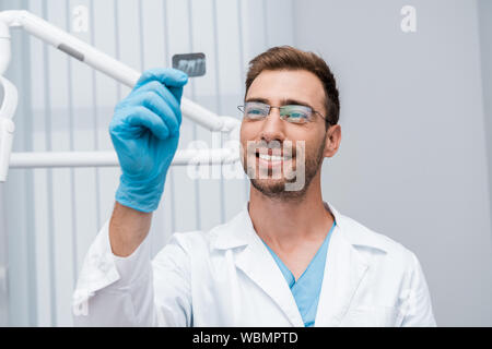 Messa a fuoco selettiva di allegro dentista in bicchieri azienda x-ray in clinica Foto Stock