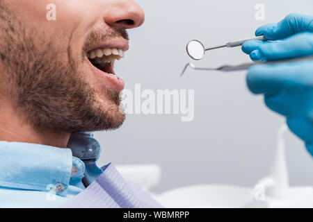 Vista ritagliata della donna in guanti in lattice azienda strumenti odontoiatrici vicino al paziente Foto Stock