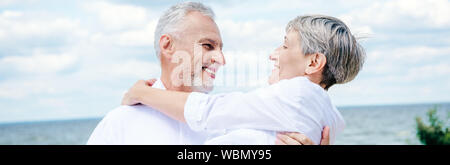 Vista panoramica di sorridere senior uomo moglie di sollevamento sotto il cielo blu Foto Stock