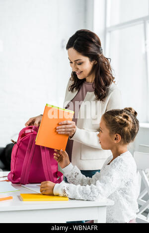 Felice madre libro mettendo in uno zaino di schoolgirl a casa Foto Stock