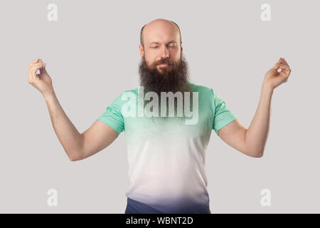 Ritratto di calma rilassante di mezza età uomo calvo con barba lunga in verde chiaro t-shirt in piedi con gli occhi chiusi, braccia sollevate e fare yoga meditazione. Foto Stock