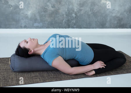 Donna Cauacasian appoggiata in eroe reclinabili porre o Supta Virasana con il piano di appoggio, stretching dopo la pratica. Studio shot Foto Stock