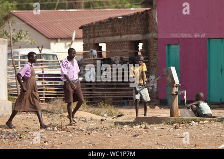 TORIT, SUD SUDAN-febbraio 20, 2013: i bambini non identificato di pompare acqua da un pozzo in Sud Sudan mentre gli studenti a piedi da Foto Stock