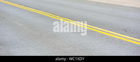 Coppia di linee gialle su grigio asfalto inclinato diagonalmente. Foto Stock