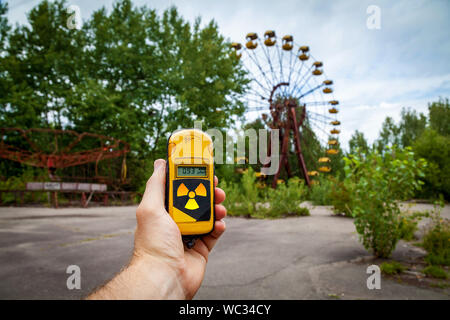 Un dosimetro in mani con un livello di radioattività in un parco giochi abbandonato nel centro di pripjat, in Chernobyl zona di esclusione, Ucraina Foto Stock