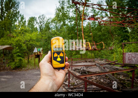 Un dosimetro in mani con un livello di radioattività in un parco giochi abbandonato nel centro di pripjat, in Chernobyl zona di esclusione, Ucraina Foto Stock