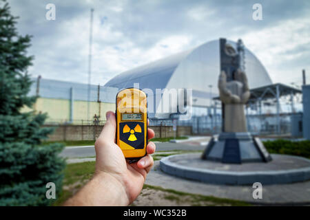 Un dosimetro in mani con un livello di radioattività vicino al monumento al Chernobyl liquidatori in prossimità del quarto reattore. Disastro di Chernobyl storia. L Foto Stock