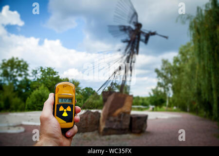 Il dosimetro in mani con un livello di radioattività nei pressi del monumento in memoria dell'incidente di Chernobyl. Disastro di Chernobyl storia. Perso il posto in Ukrain Foto Stock