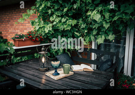 Balcone privato all'aperto con vitigni decorativo salendo sulla parete, marrone mobili da giardino, tazza di bevanda, i cookie. Modern dark Instagram stili di vita Foto Stock