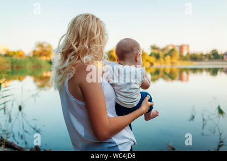 Giovane madre a piedi dal fiume estate con baby girl. La donna mostra natura orizzontale per il suo bambino. La famiglia trascorre del tempo insieme Foto Stock