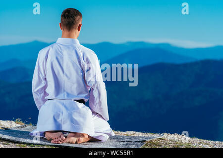 Karate master meditando sulla cima di una montagna di indossare il kimono mentre guardando giù al lago di montagna. Foto Stock