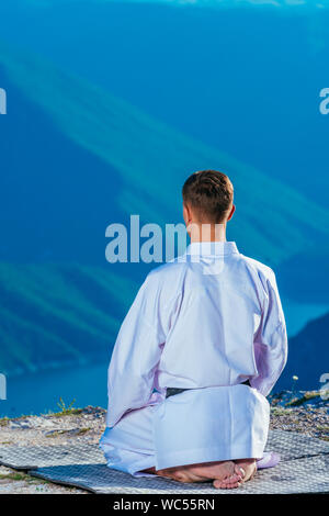 Karate master meditando sulla cima di una montagna di indossare il kimono mentre guardando giù al lago di montagna. Foto Stock