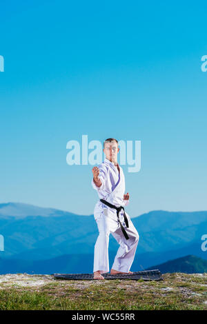 Bionda atleta di karate non kata sulla cima di una montagna mentre si esegue una linea di calci, pugni e blocchi sulla cima di una montagna in una giornata di sole. Foto Stock