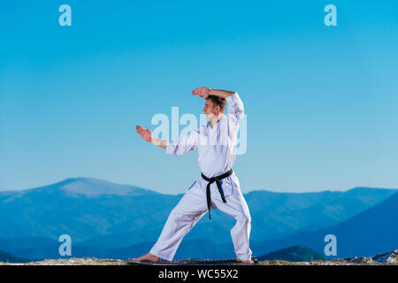 Bionda atleta di karate non kata sulla cima di una montagna mentre si esegue una linea di calci, pugni e blocchi sulla cima di una montagna in una giornata di sole. Foto Stock