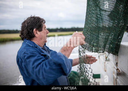 Pescatore commerciale riassettavano le reti sul ponte di una barca da pesca Foto Stock