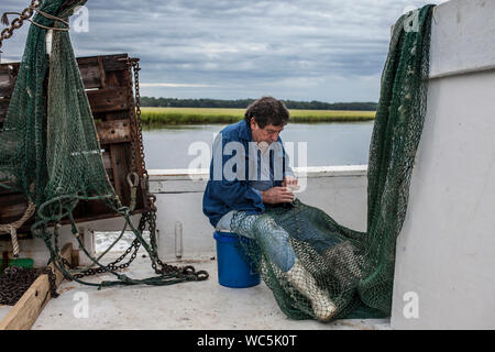 Pescatore commerciale mende la sua rete sul ponte di una nave Foto Stock