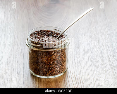 Materie semi di lino in un vasetto di vetro con cucchiaio di metallo su un tavolo di legno. Cibo sano per abbassare il colesterolo e prevenire le malattie cardiache e il cancro. Foto Stock