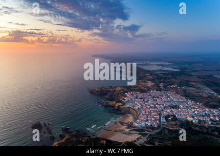 Vista aerea del Zambujeira do Mar villaggio e la spiaggia al tramonto, in Alentejo, Portogallo; Foto Stock