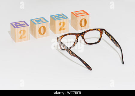 Anno 2020 stabiliti con cubetti di giocattolo con i numeri accanto ai bicchieri su bianco Foto Stock