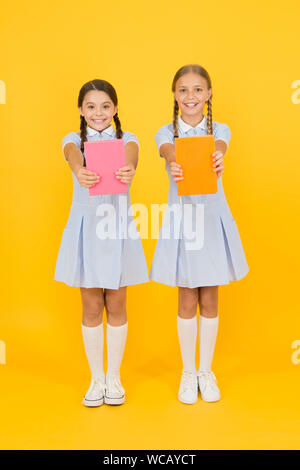 Biblioteca Scolastica. Concetto di homeschooling. Club di alfabetizzazione. Carino bambini azienda libri su sfondo giallo. Bambine con enciclopedia o libri per bambini. Libri educativi per le scuole. La lettura di libri. Foto Stock