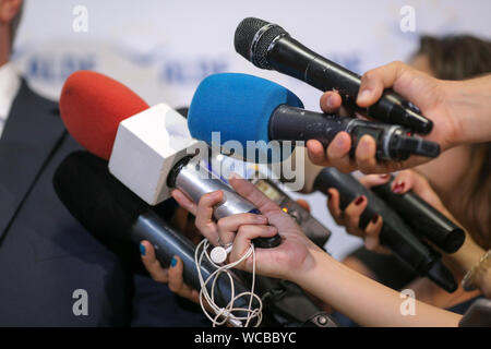 Dettagli con le mani dei giornalisti holding usurati microfoni davanti a un candidato durante una conferenza stampa Foto Stock