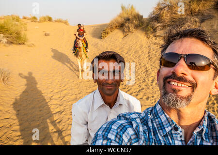 Un turista caucasica su un cammello trek prende un selfie di se stesso e il suo autista come pure sua moglie sul suo cammello con il suo autista in background. Foto Stock