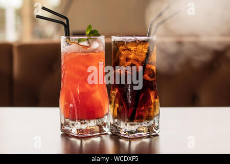 Due bicchieri di cocktail con ghiaccio e cannucce sul tavolo. Fresca bevanda fredda con limone. Arancio brillante cocktail. Liquido trasparente giallo. Congelati. Foto Stock